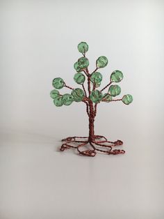 a wire tree with green glass leaves on it's branches and roots, in front of a white background