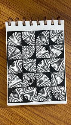 a spiral notebook with black and white designs on the cover sitting on a wooden table