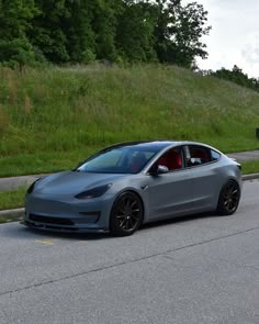 a grey car is parked on the side of the road next to a grassy hill