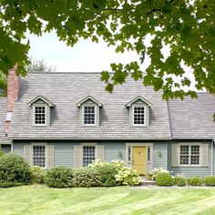 a blue house with two windows and a yellow door in front of some green grass