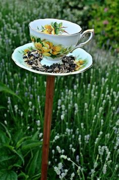 a teacup and saucer on a stand in the middle of a garden filled with wildflowers