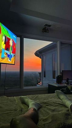 a person laying on top of a bed in front of a large window with a tv