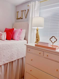 a white bed sitting next to a window with pink pillows on top of it in a bedroom