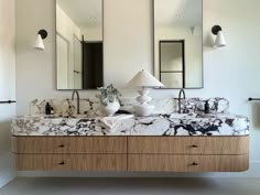 a bathroom with marble counter tops and two mirrors on the wall, along with lamps