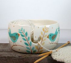 a yarn bowl with two birds painted on it next to a crochet hook