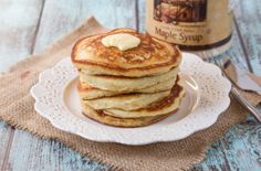 a stack of pancakes on a plate next to a jar of maple syrup and spoon