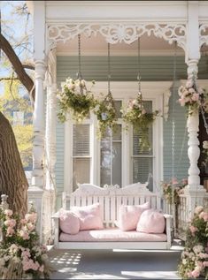 a white porch swing with pink pillows and flowers on the front, along with greenery