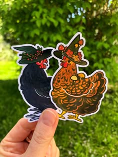 a hand holding up a sticker with two roosters on it