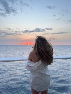 a woman standing on the deck of a ship looking out at the ocean as the sun sets