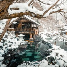 a snow covered forest with a small stream running through the center and a wooden cabin in the background