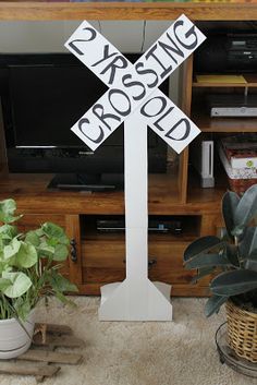 a white cross sign sitting on top of a wooden table next to a potted plant