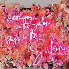 pink flowers and neon signs on a wall with the words what happens in the salon stays in the salon