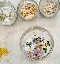 four glass bowls filled with different types of herbs and seasonings on a white surface