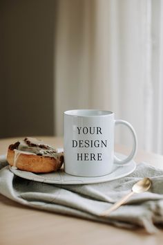 a white coffee mug sitting on top of a table next to a piece of bread