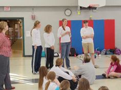 a group of people standing around in a gym with one person on the floor talking