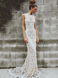 a woman standing in front of a stone wall wearing a white dress with flowers on it