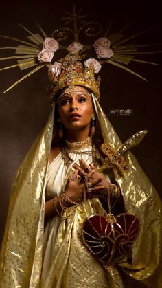 a woman dressed in gold and holding a heart with flowers on it's head