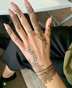 a woman's hand with henna tattoos on her left arm and wrist, sitting in front of a table