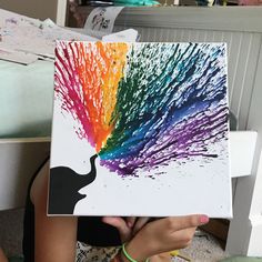 a person sitting on the floor holding up a painting with paint splatters all over it