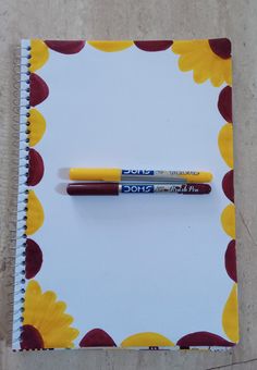 two pens sitting on top of a spiral bound notepad next to a flowered notebook