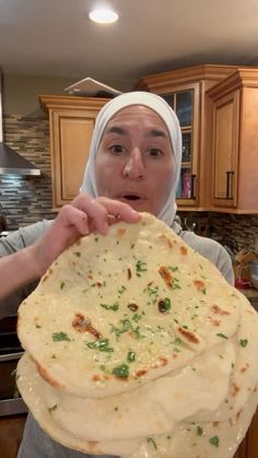 a woman in a headscarf holds up a stack of flatbreads