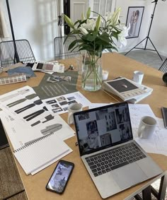 an open laptop computer sitting on top of a wooden table next to a vase filled with flowers