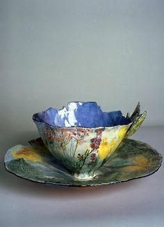 a bowl on a saucer with flowers painted on the bottom and sides, sitting on a plate