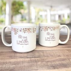 two white coffee mugs sitting on top of a wooden table next to each other