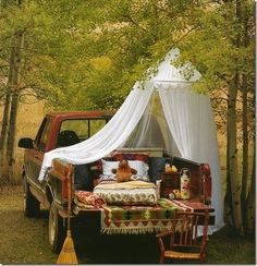 a bed sitting in the middle of a forest next to a truck