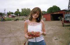 a woman holding strawberries in her hands while standing next to a horse pen and barn