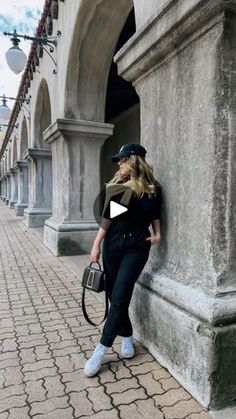 a woman leaning up against a wall with her hand on the back of her purse