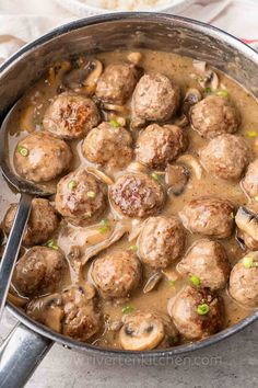 meatballs and mushrooms are being cooked in a pot with a ladle on the side