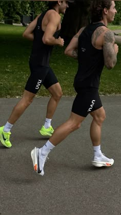 two men running in the street wearing black and neon green shorts, one with tattoos on his arm