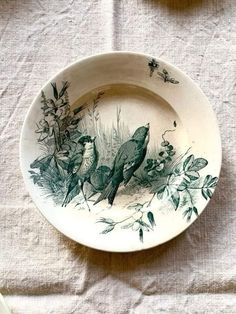 a plate with birds painted on it sitting on a white table cloth next to other plates