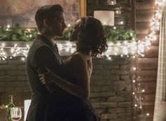 a man and woman standing next to each other in front of a fireplace with christmas lights