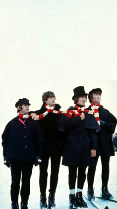 four men standing in the snow with hats and scarves around their necks, all wearing skis