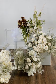 three vases filled with white flowers on top of a wooden floor next to each other