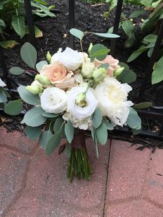 a bridal bouquet sitting on the ground in front of a black iron fence with greenery