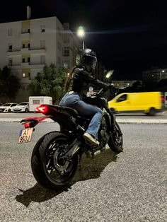 a man riding on the back of a motorcycle down a street at night with traffic behind him