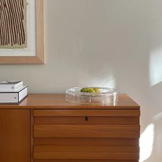 a bowl of fruit sitting on top of a wooden dresser next to a framed painting