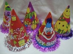 three birthday hats with purple tinsel on them, one has clown faces and the other has happy birthday written on it