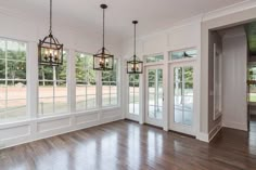 an empty living room with wood floors and large windows, chandeliers hanging from the ceiling