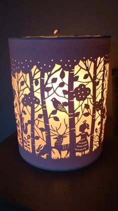 a lit candle that is on top of a table with trees and animals in it