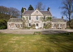 a large stone house sitting in the middle of a lush green field with lots of trees