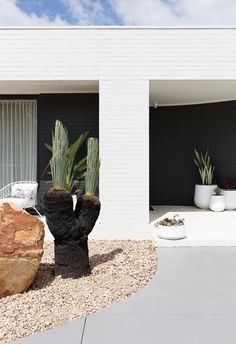 a white house with two large rocks in front of it and plants on the side