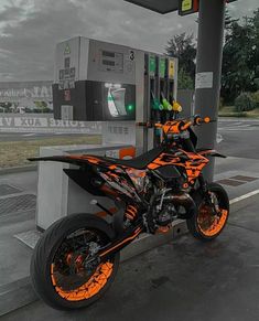 an orange and black motorcycle parked next to a gas station pump with nozzles