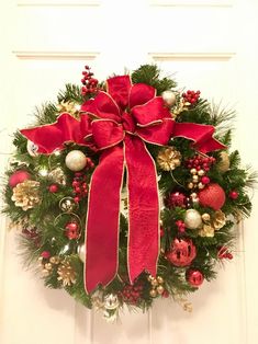 a christmas wreath on the front door with red bows and ornaments hanging from it's sides