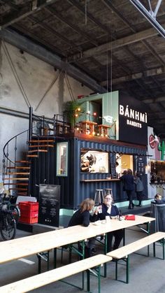 two people sitting at tables in front of a building that has an open air cafe