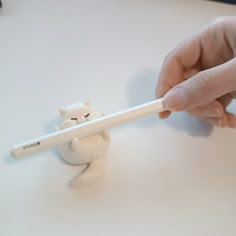 a person is holding a white pen in front of a cat figurine on a table