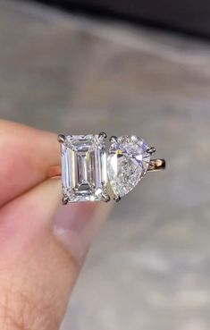 an engagement ring with two pear shaped diamonds on it's side, in someone's hand